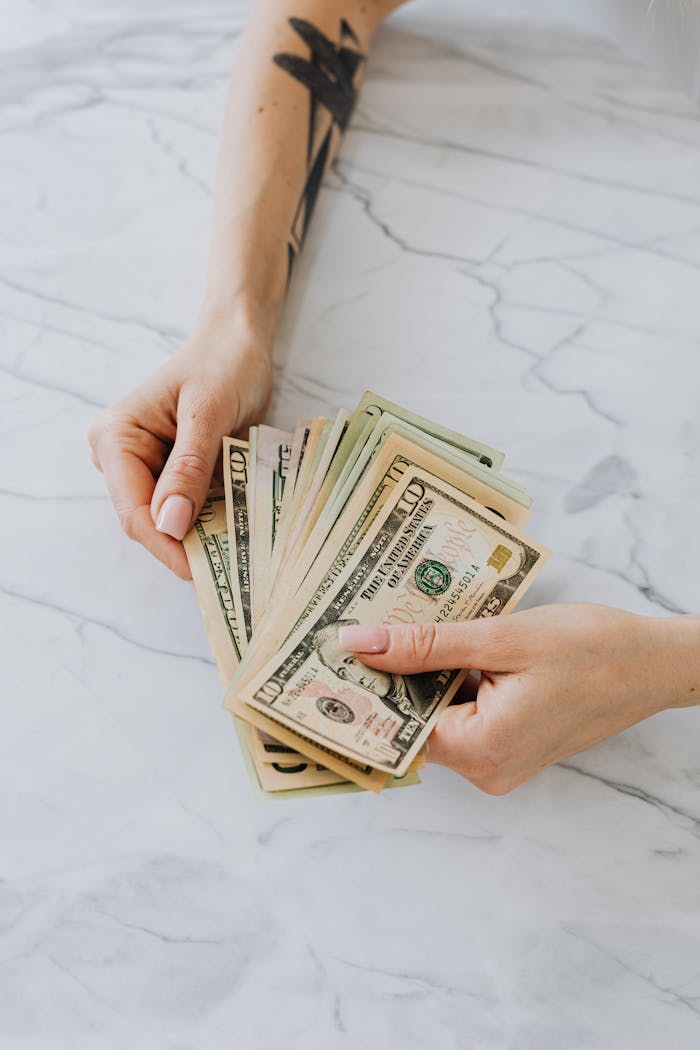 Hands holding a fan of US dollar bills on a marble table, symbolizing wealth and finance.